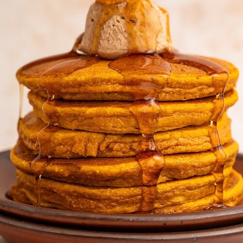 Stack of golden pumpkin protein pancakes with cinnamon butter and maple syrup drizzling down