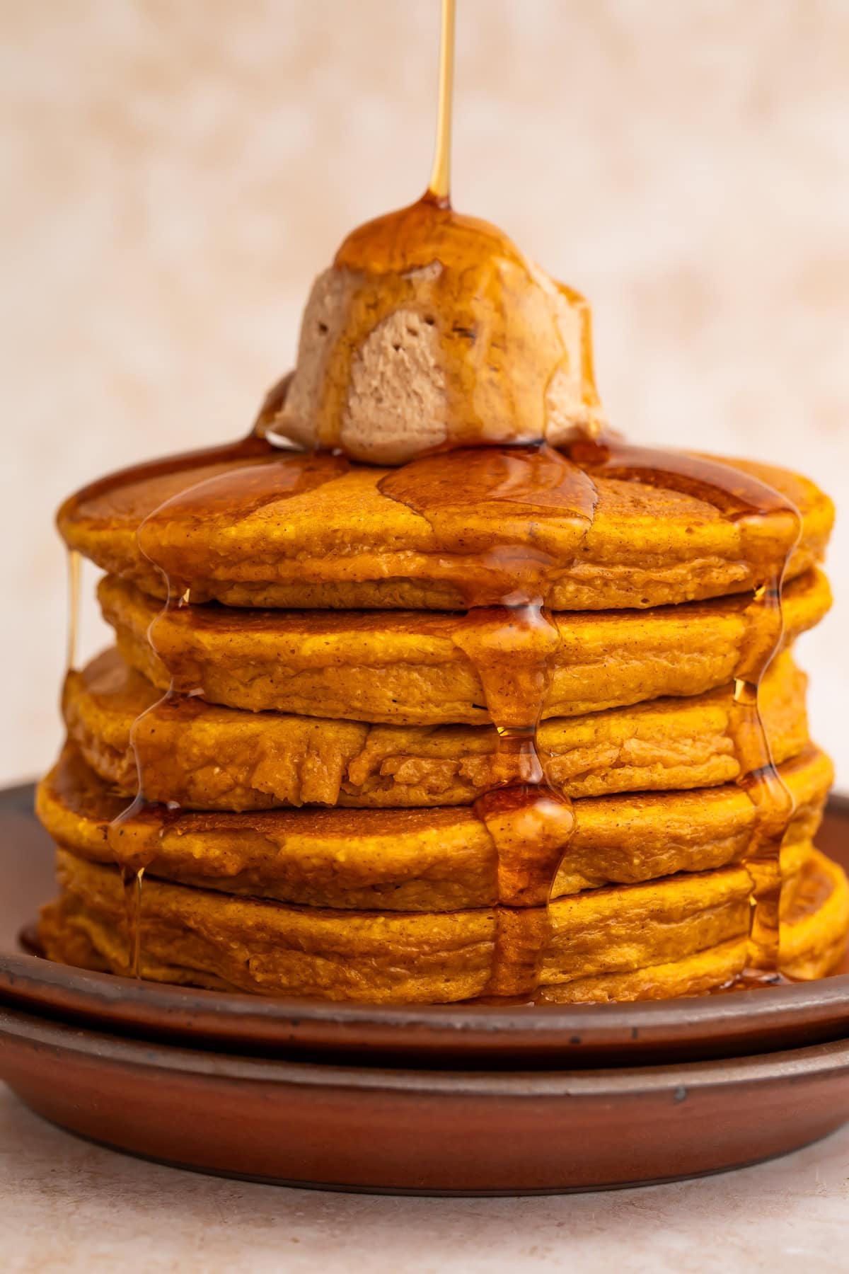 Stack of golden pumpkin protein pancakes with cinnamon butter and maple syrup drizzling down