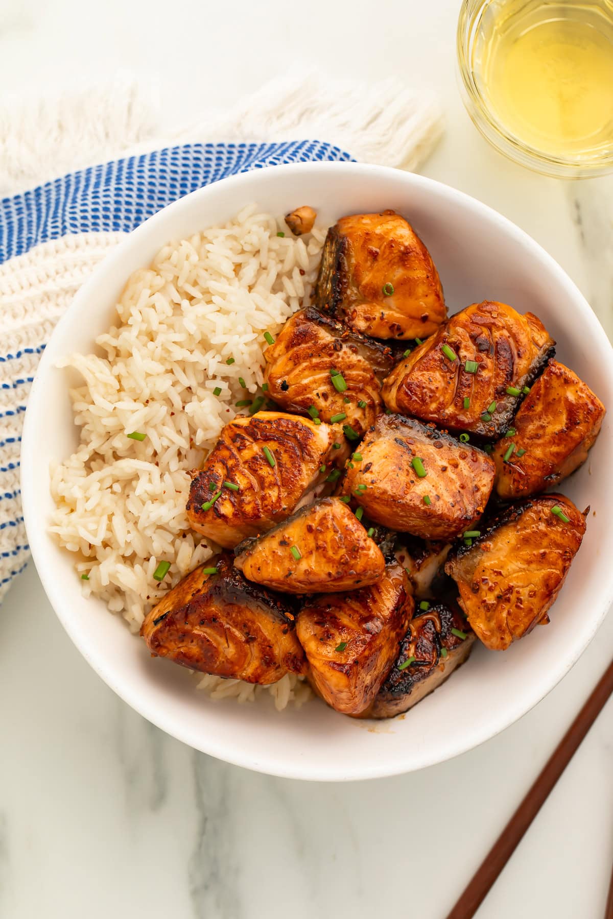 Hot honey salmon bites and rice in white bowl with glass of white wine