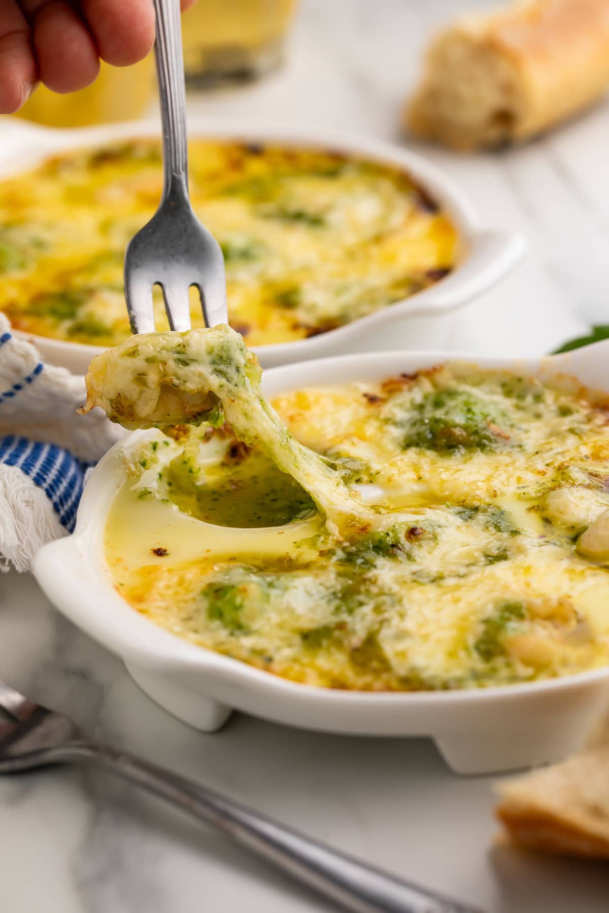 Fork lifting a bite of lobster escargot with melted cheese stretching