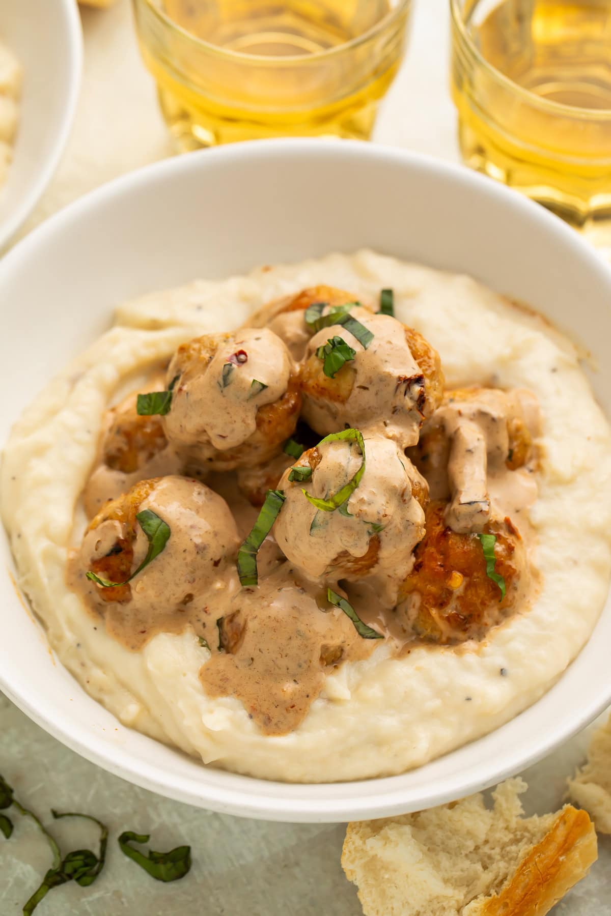 Marry me chicken meatballs served over creamy mashed potatoes in white bowls with wine glasses