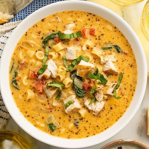Marry Me Chicken Soup in white bowls with ditalini pasta, chunks of chicken, sun-dried tomatoes, and fresh basil garnish, served with white wine