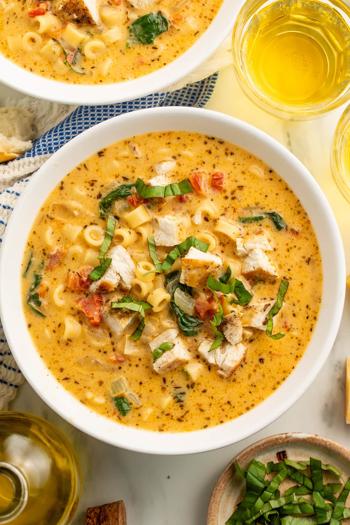 Marry Me Chicken Soup in white bowls with ditalini pasta, chunks of chicken, sun-dried tomatoes, and fresh basil garnish, served with white wine