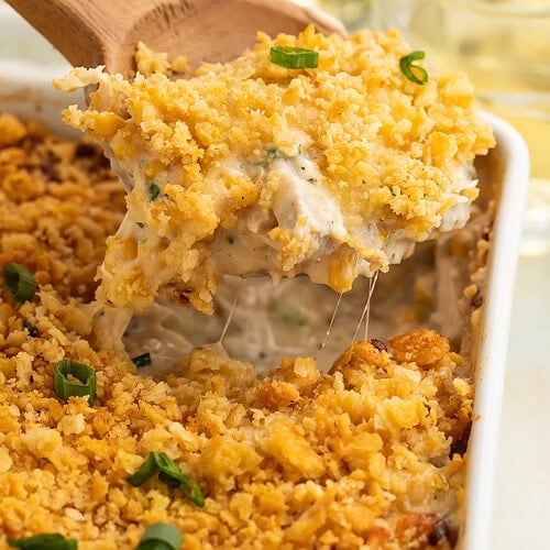 Wooden spoon lifting portion of Million Dollar Chicken Casserole showing melted cheese strings