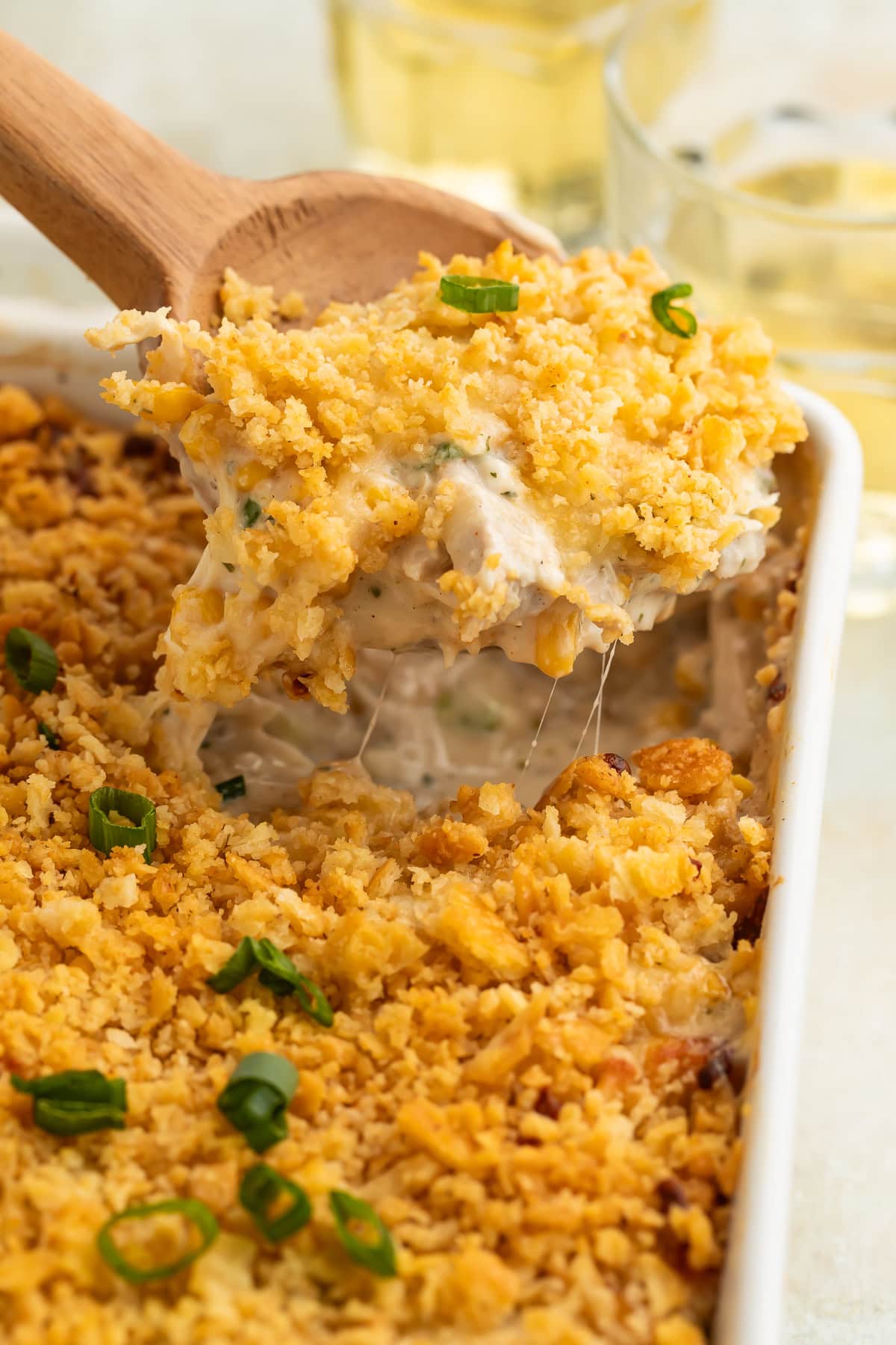 Wooden spoon lifting portion of Million Dollar Chicken Casserole showing melted cheese strings