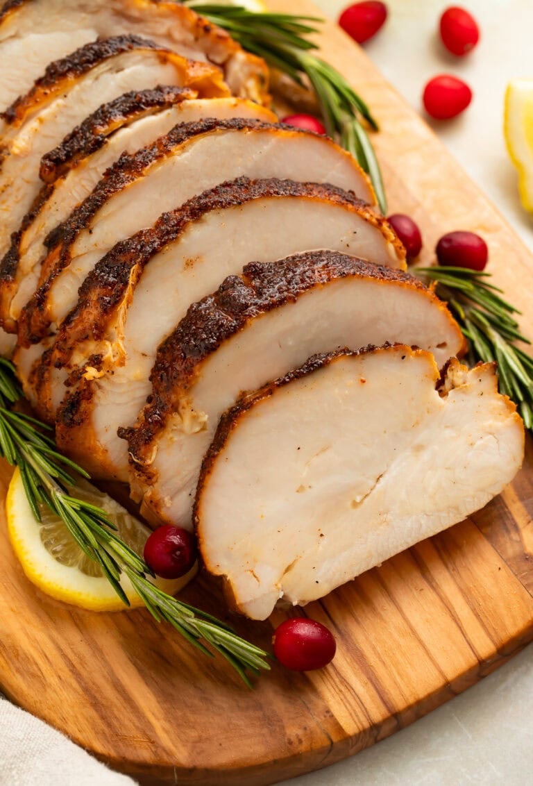Sliced smoked turkey breast with golden-brown skin on wooden cutting board with rosemary and cranberries