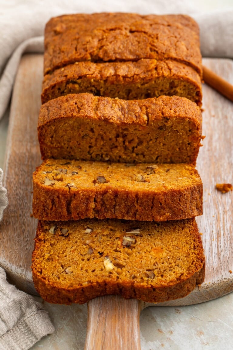 Sliced sweet potato bread with pecans on wooden cutting board showing moist orange crumb