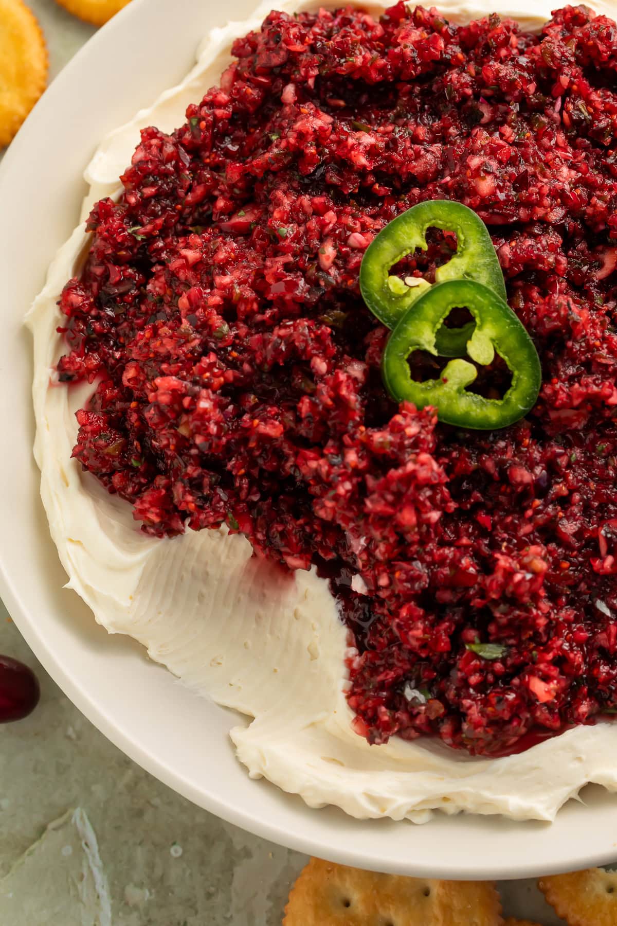 Cranberry jalapeño dip layered over cream cheese on a white plate, garnished with fresh jalapeño slices and surrounded by Ritz crackers.