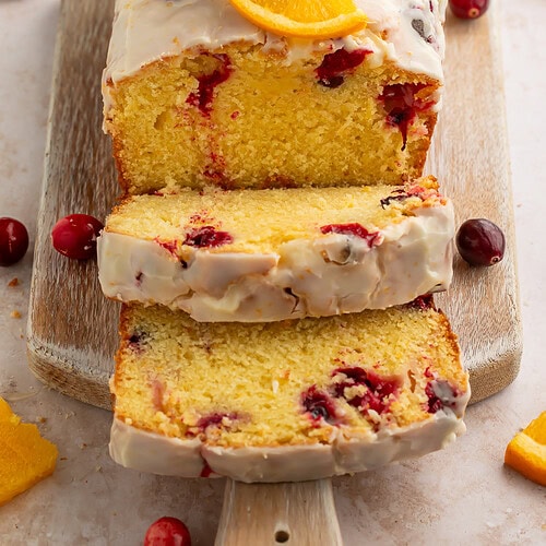 Sliced cranberry orange bread moist pieces with white glaze on wooden board showing moist crumb with whole cranberries
