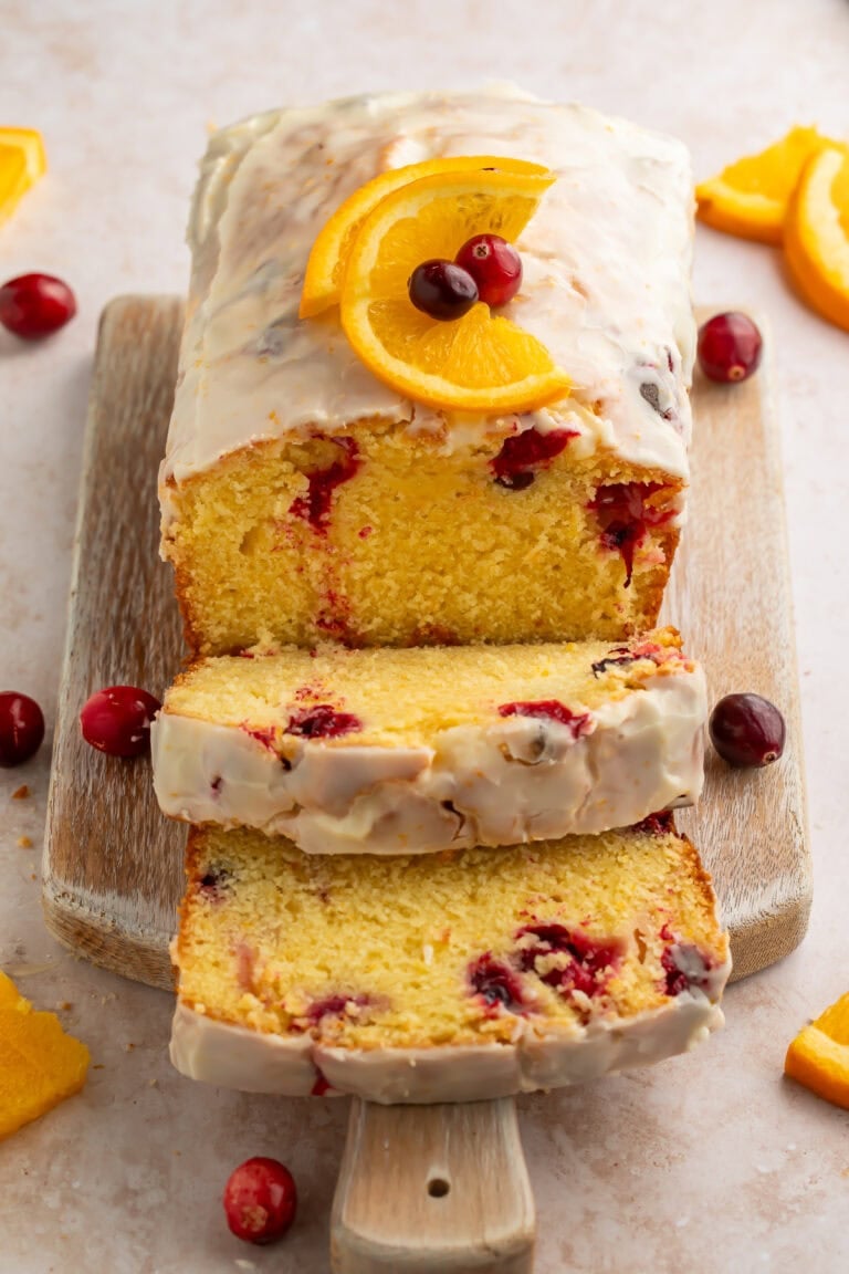 Sliced cranberry orange bread moist pieces with white glaze on wooden board showing moist crumb with whole cranberries