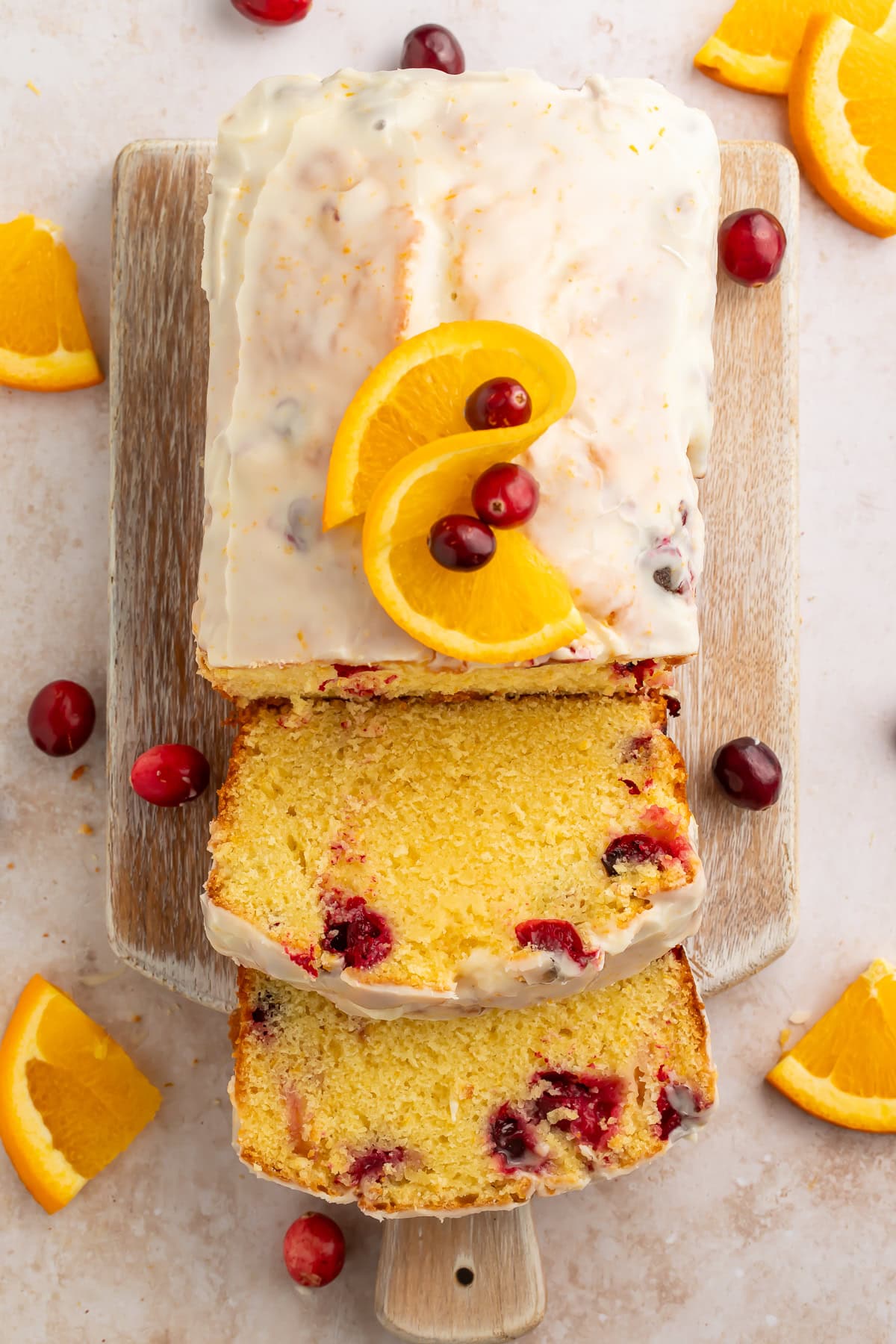 Overhead view of glazed cranberry orange bread with dried cranberries sliced on wooden cutting board with fresh orange slices