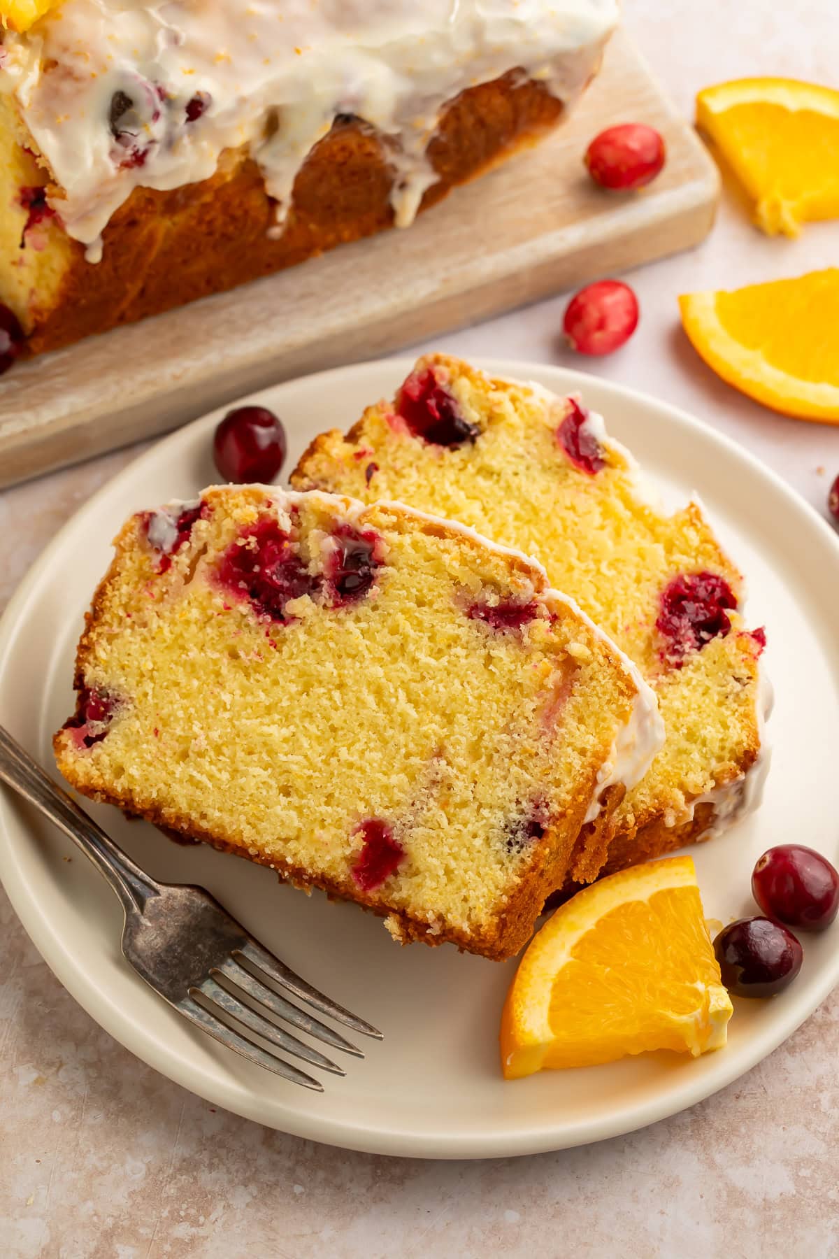 wo slices of dried cranberry and orange bread with glaze on white plate with fork and fresh orange wedge