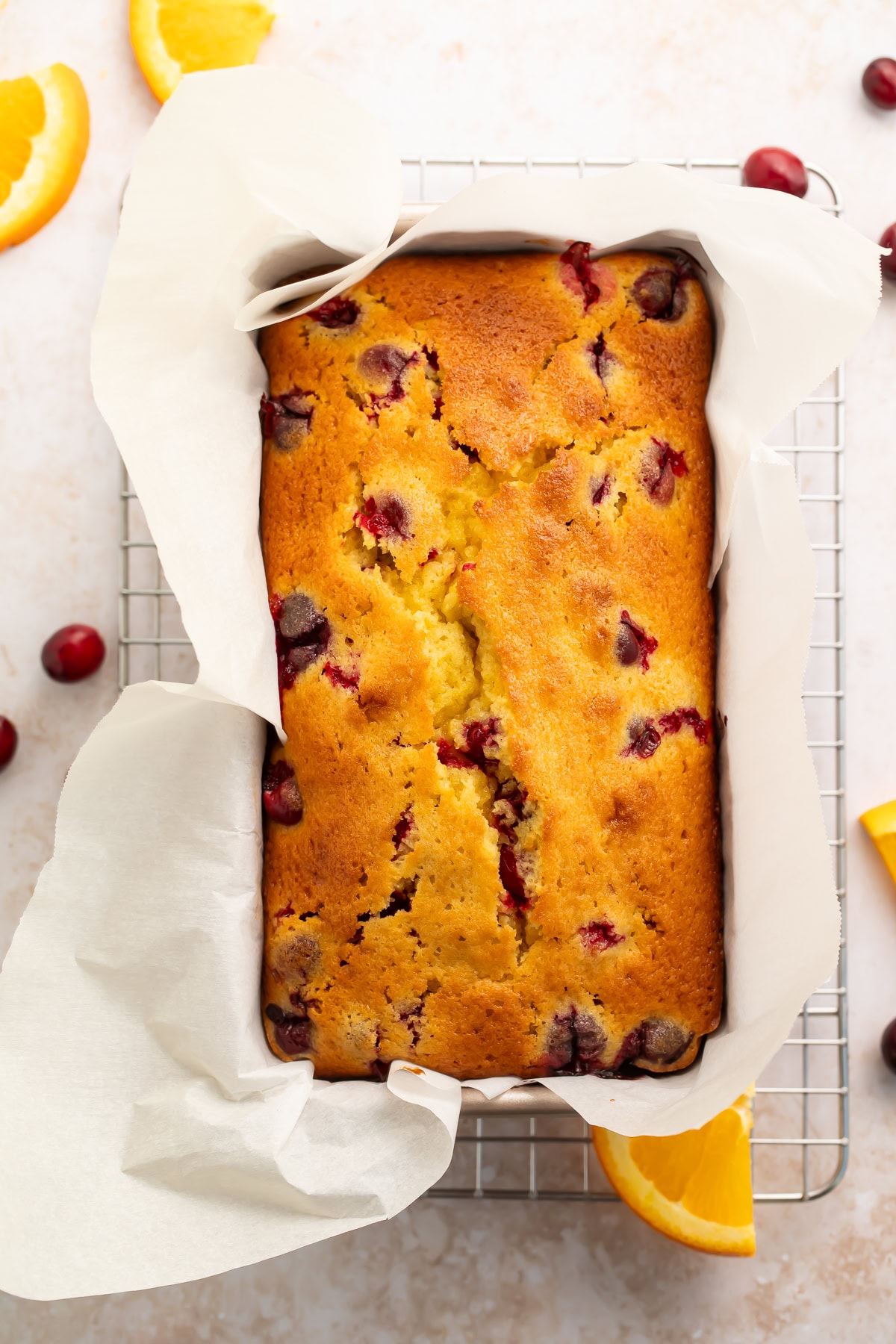 Golden brown recipe cranberry orange bread in loaf pan lined with parchment paper with fresh cranberries visible on top