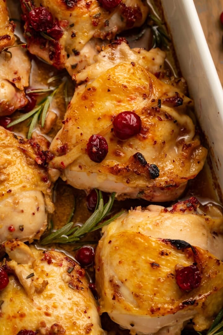 Close-up of golden-brown roasted chicken thighs with fresh cranberries and rosemary herbs