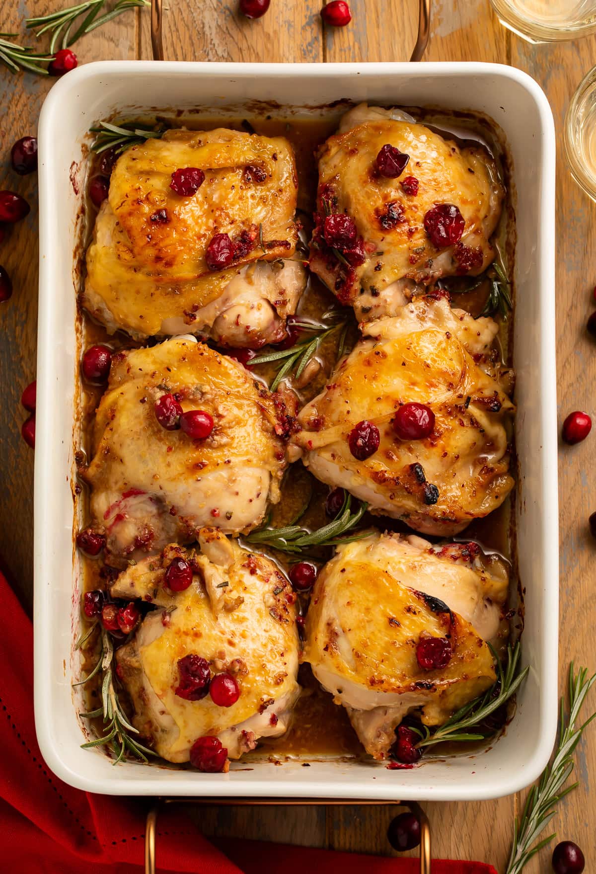 Overhead view of six roasted chicken thighs with cranberries and rosemary in white baking dish