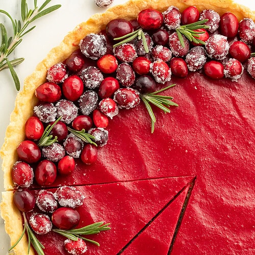 Overhead view of cranberry tart with two slices cut, showing smooth red filling and flaky crust