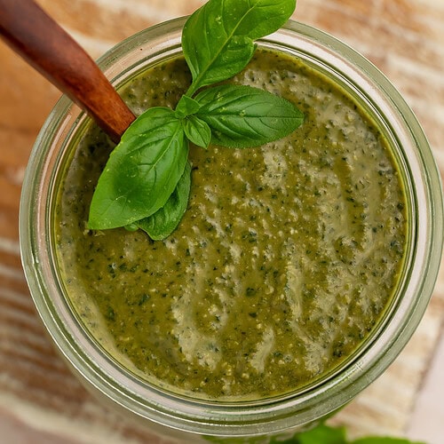 Creamy pesto sauce in a glass jar with fresh basil leaves and wooden spoon