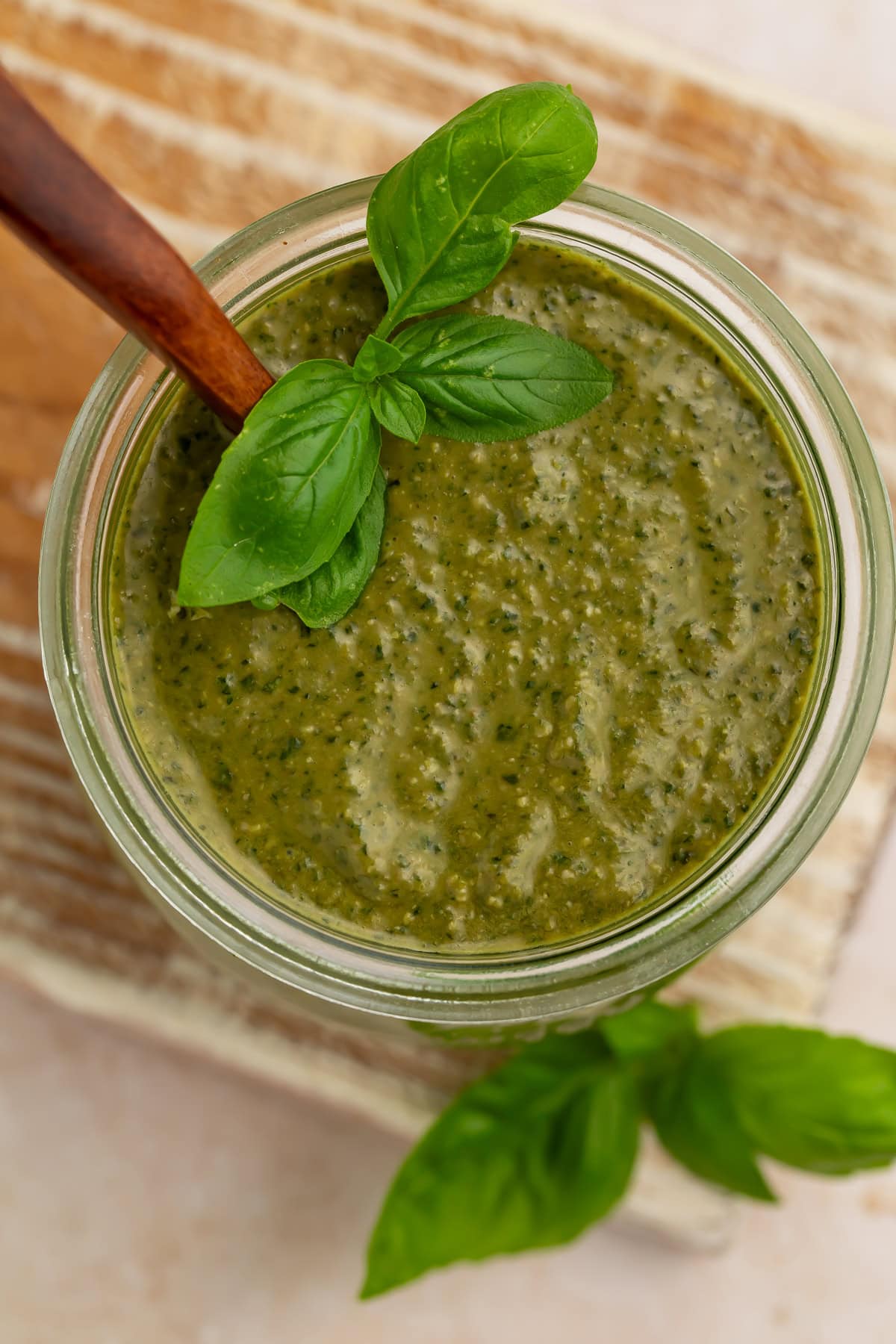 Creamy pesto sauce in a glass jar with fresh basil leaves and wooden spoon