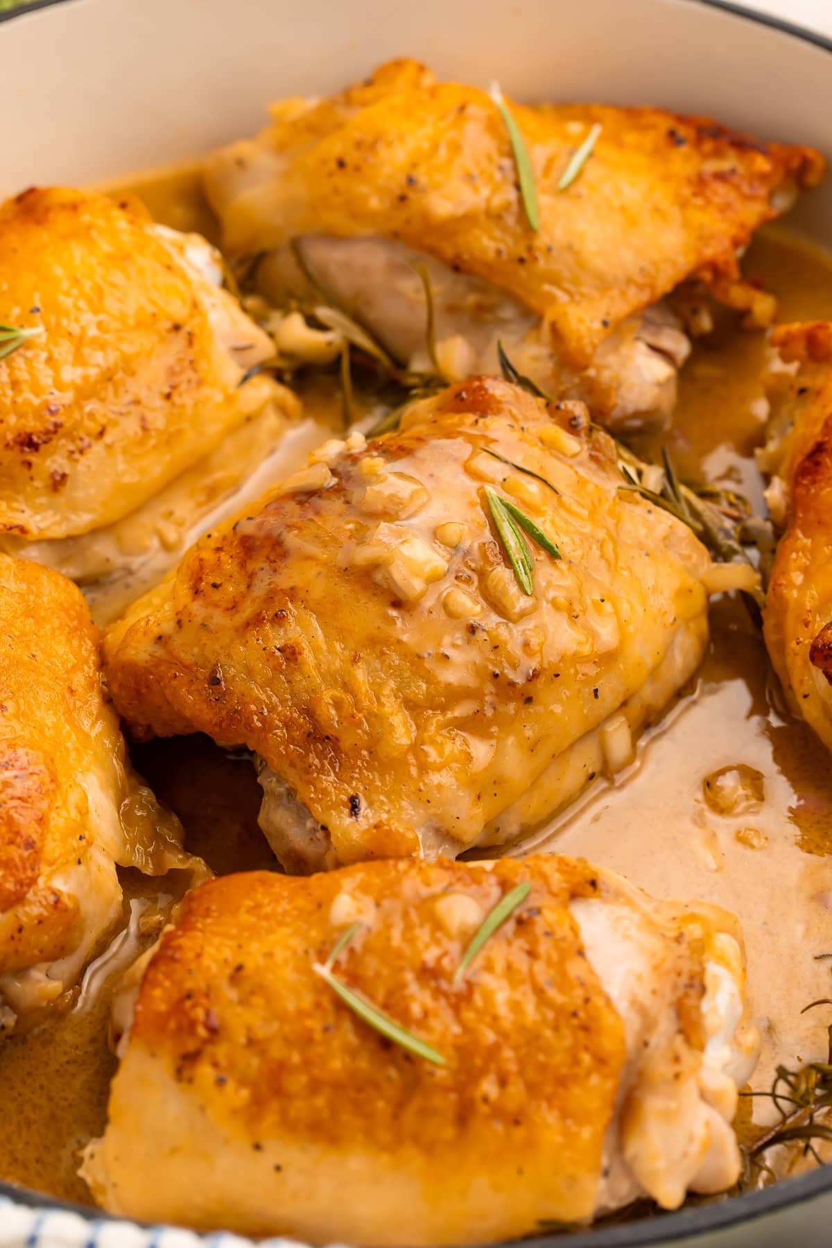 Close up overhead view of maple glazed chicken thighs with rosemary in white skillet