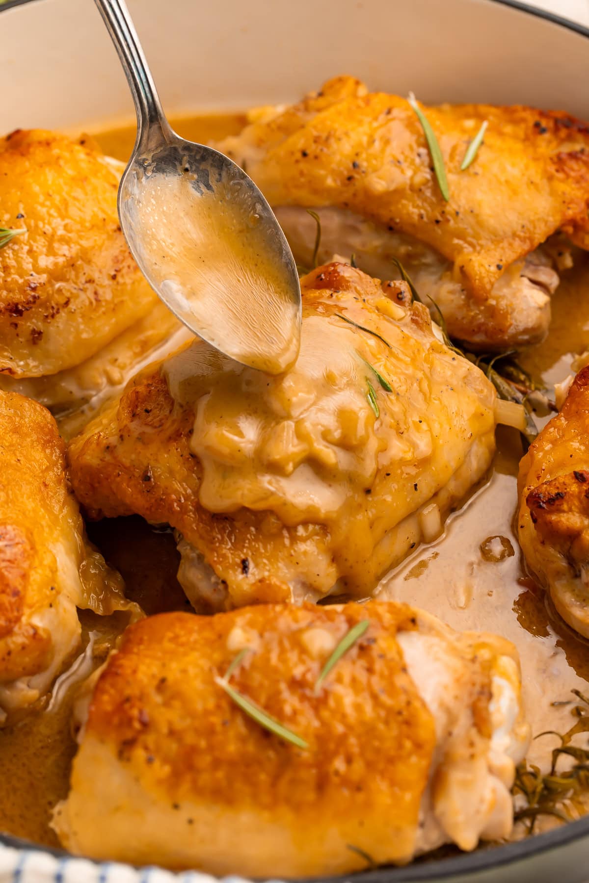 Spoon drizzling maple dijon sauce over crispy chicken thighs with rosemary