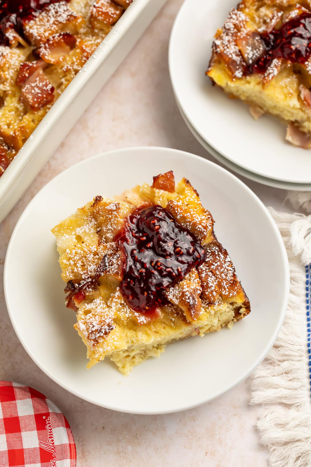 Slice of Monte Cristo breakfast casserole on a white plate topped with raspberry jam and powdered sugar.