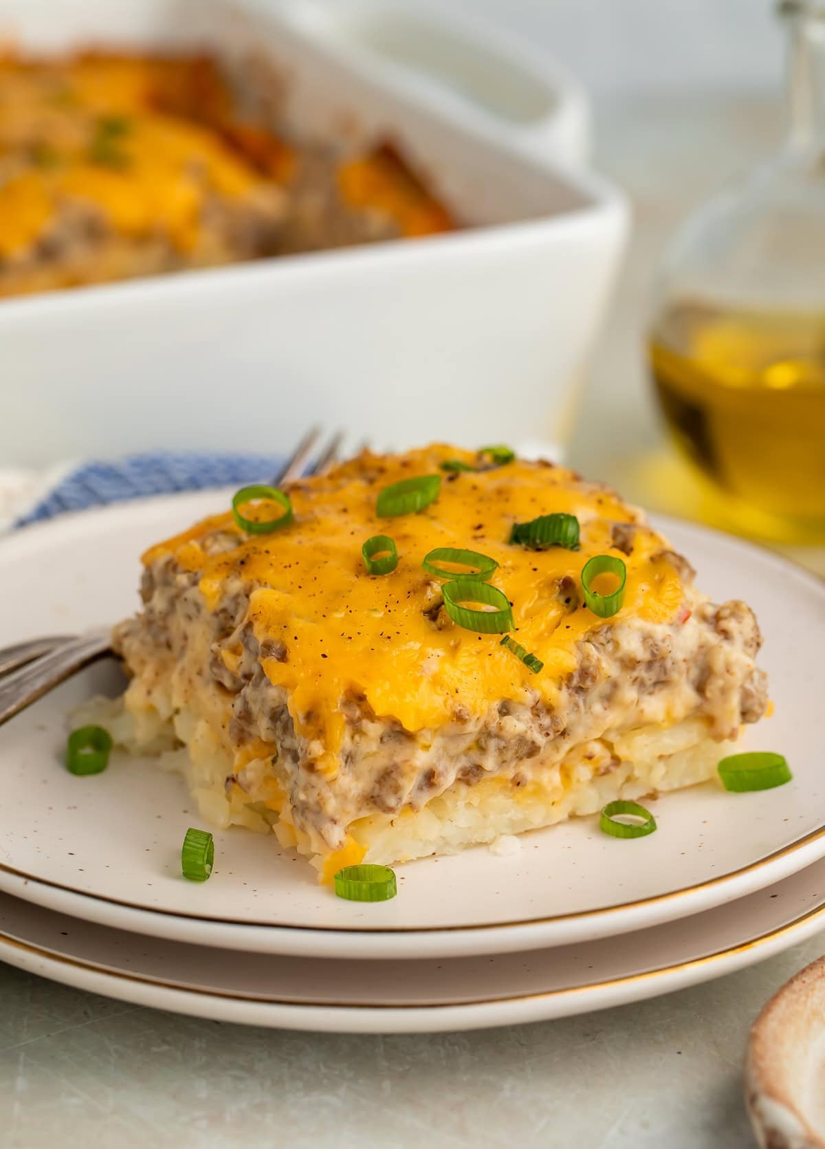 Slice of sausage hashbrown breakfast casserole on white plate showing creamy layers with green onion garnish