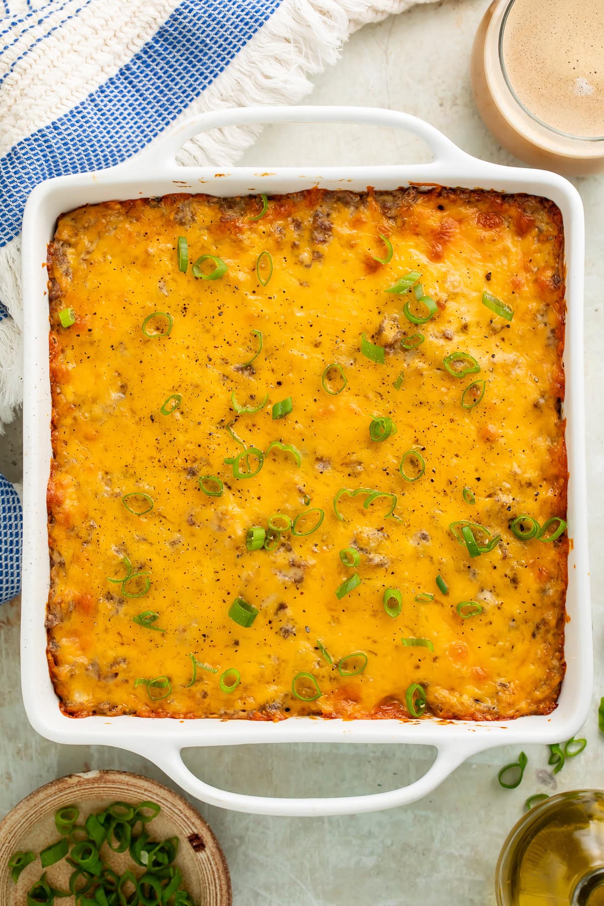 Breakfast casserole with cheese and green onions in white square baking dish with coffee and kitchen towel