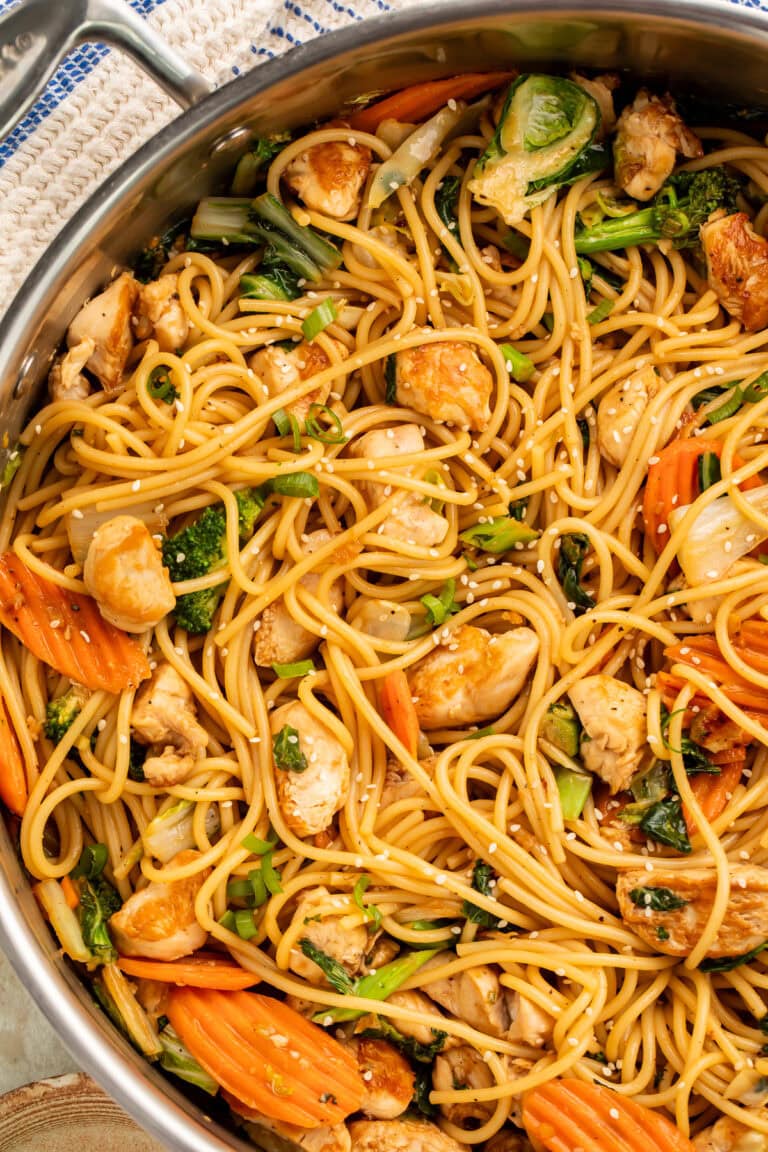 Sesame garlic chicken lo mein in a large skillet with noodles, broccoli, carrots, and chicken topped with sesame seeds
