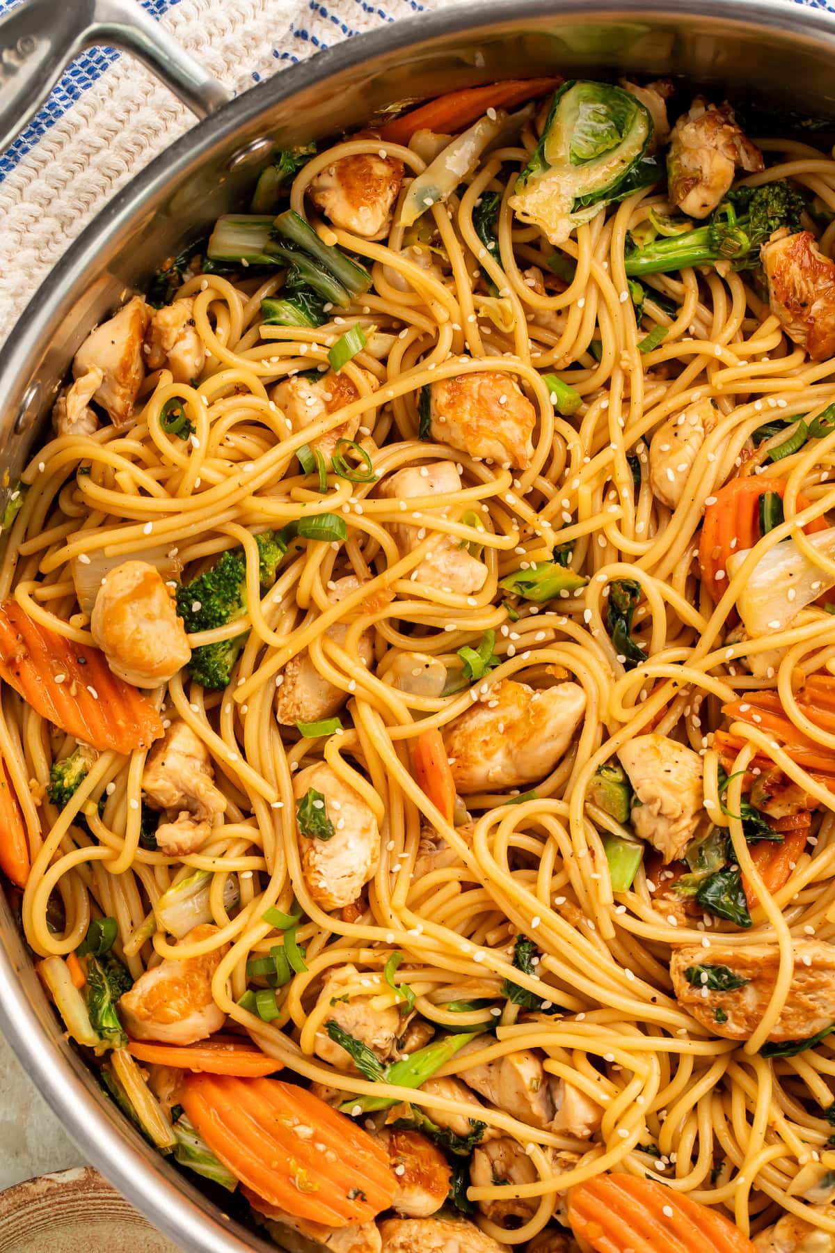 Sesame garlic chicken lo mein in a large skillet with noodles, broccoli, carrots, and chicken topped with sesame seeds