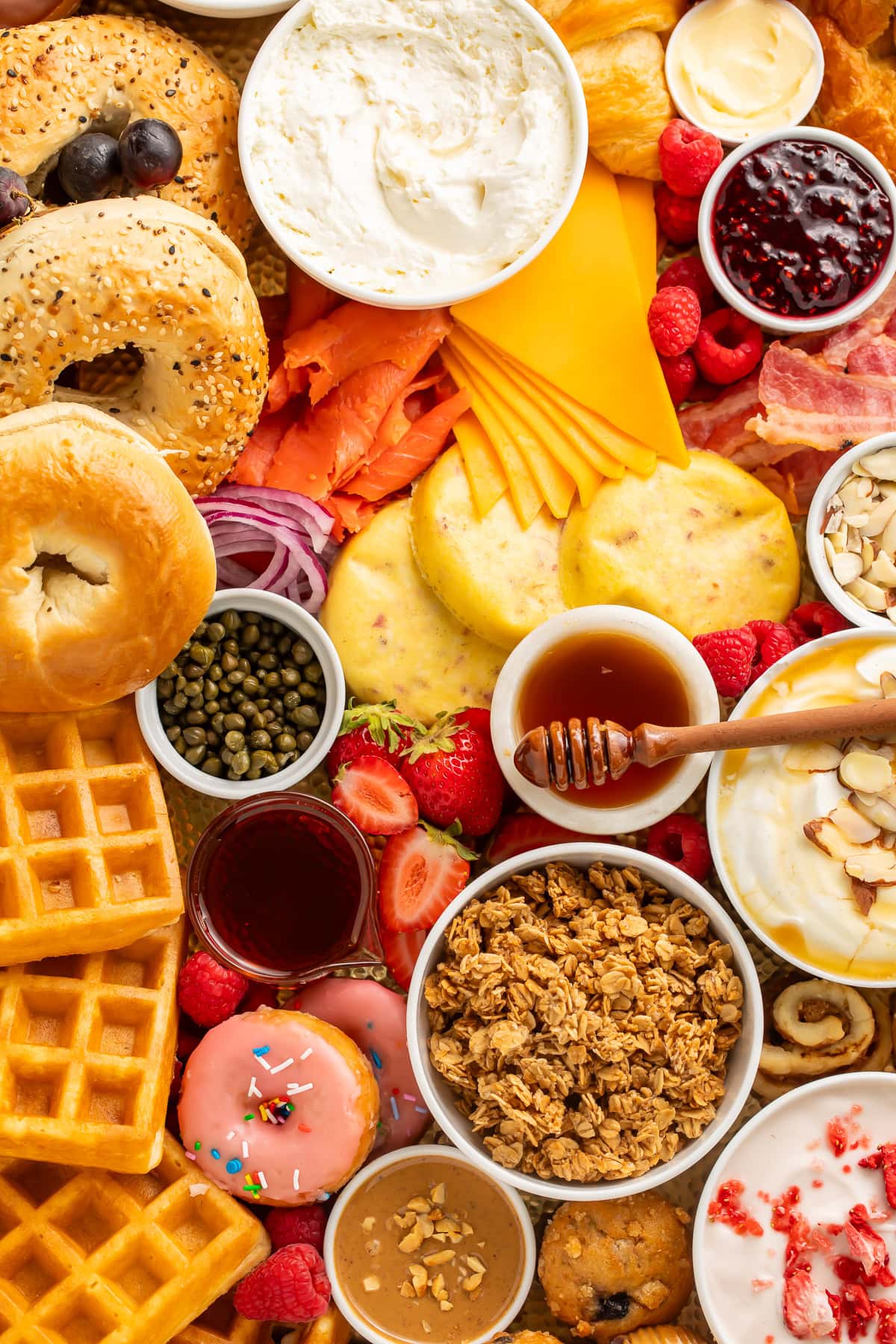 Overhead view of breakfast charcuterie board corner with bagels, cream cheese, smoked salmon, waffles, cheese, and fresh berries.