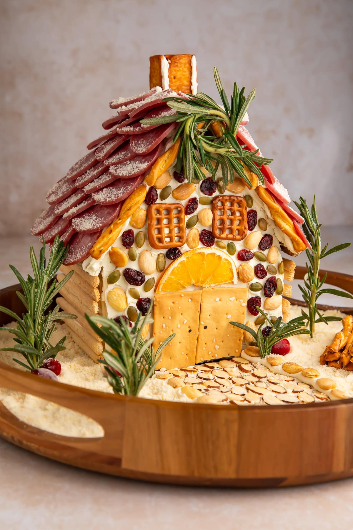 Close-up of charcuterie chalet showing salami roof shingles, pretzel chimney, and decorative nuts and cranberries on facade.