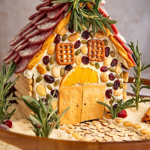 Detailed view of charcuterie chalet with cream cheese mortar, crackers as windows, and rosemary tree garnishes.