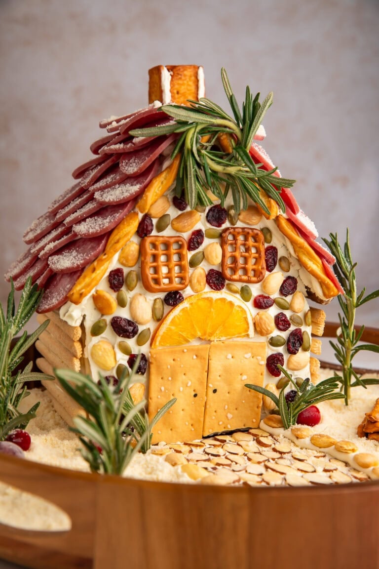 Detailed view of charcuterie chalet with cream cheese mortar, crackers as windows, and rosemary tree garnishes.