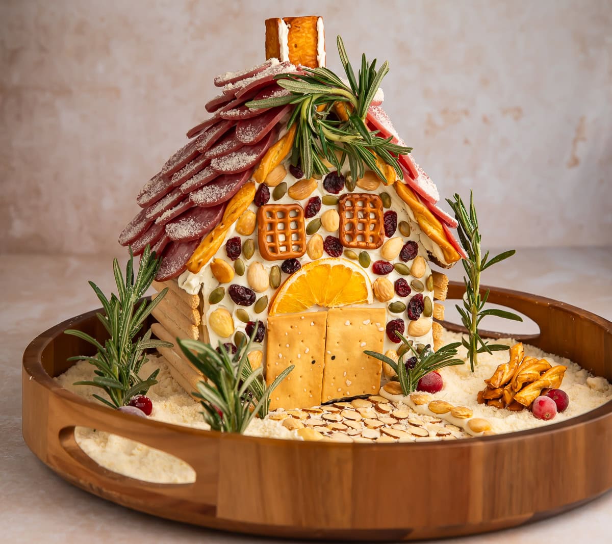 Full view of Christmas charcuterie chalet on wooden lazy Susan with salami roof and festive decorations.