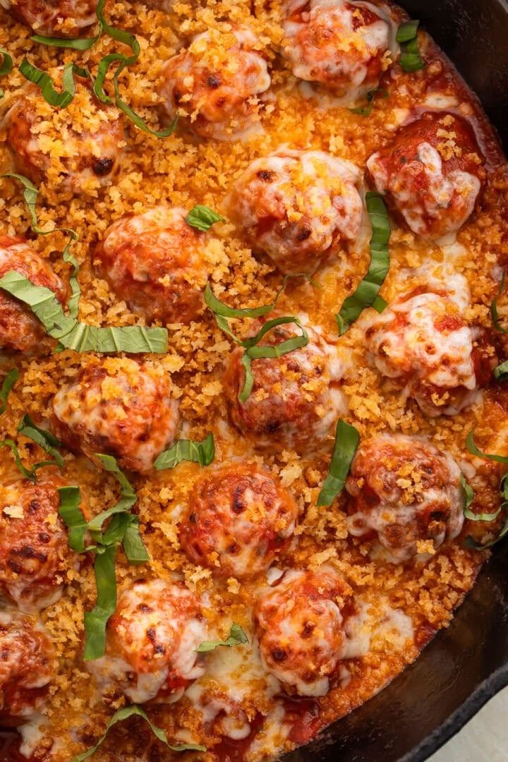 Overhead view of chicken parmesan meatballs in cast iron skillet with melted mozzarella, golden breadcrumbs, and fresh basil.