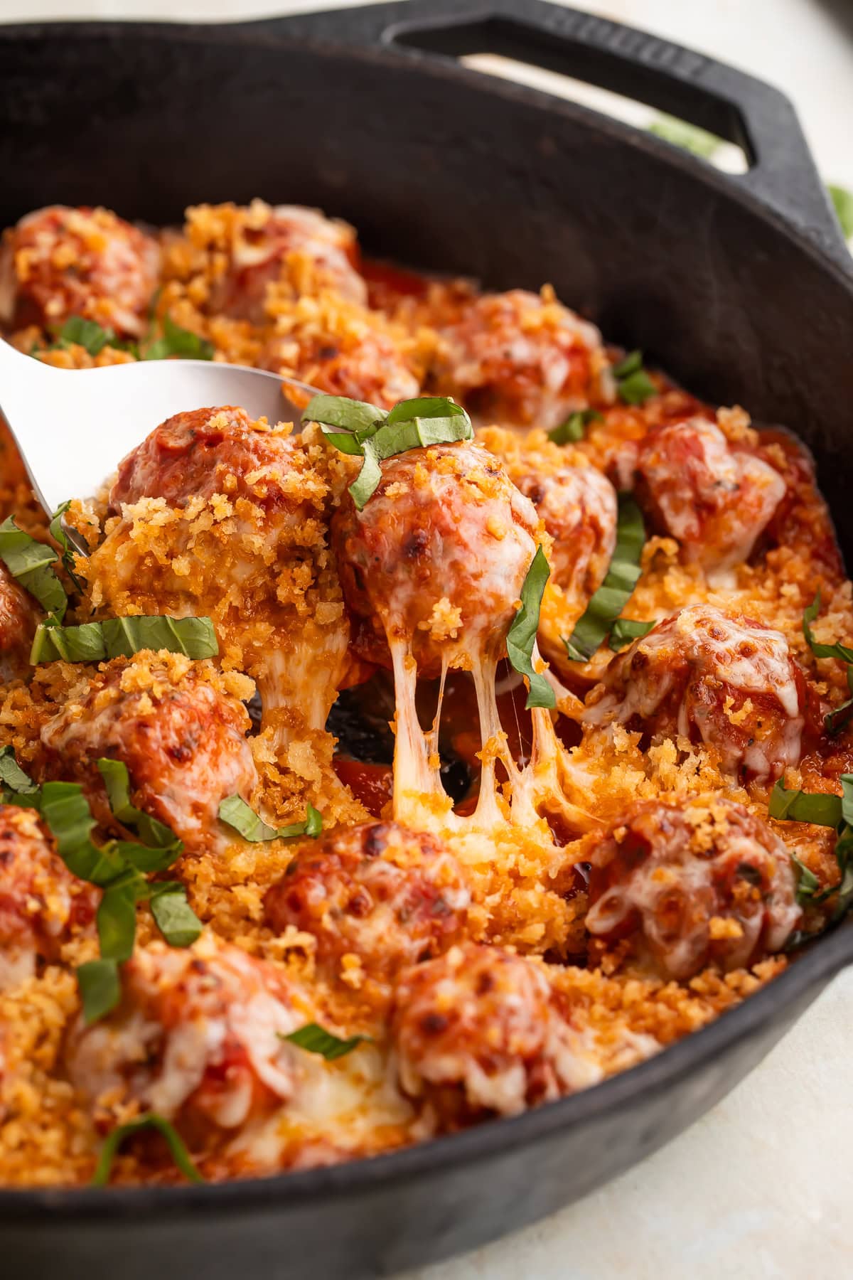 Chicken parmesan meatball being lifted from cast iron skillet with melted mozzarella cheese stretching from the pan.