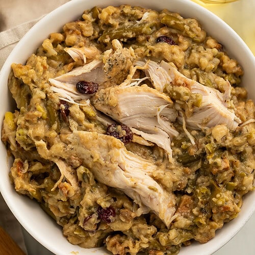 White bowl filled with shredded chicken and herb stuffing with green beans and dried cranberries on wooden table