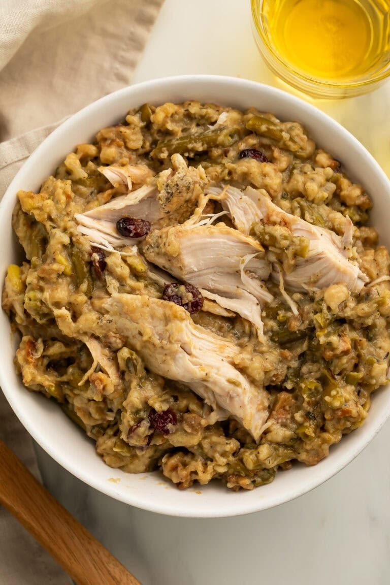 White bowl filled with shredded chicken and herb stuffing with green beans and dried cranberries on wooden table