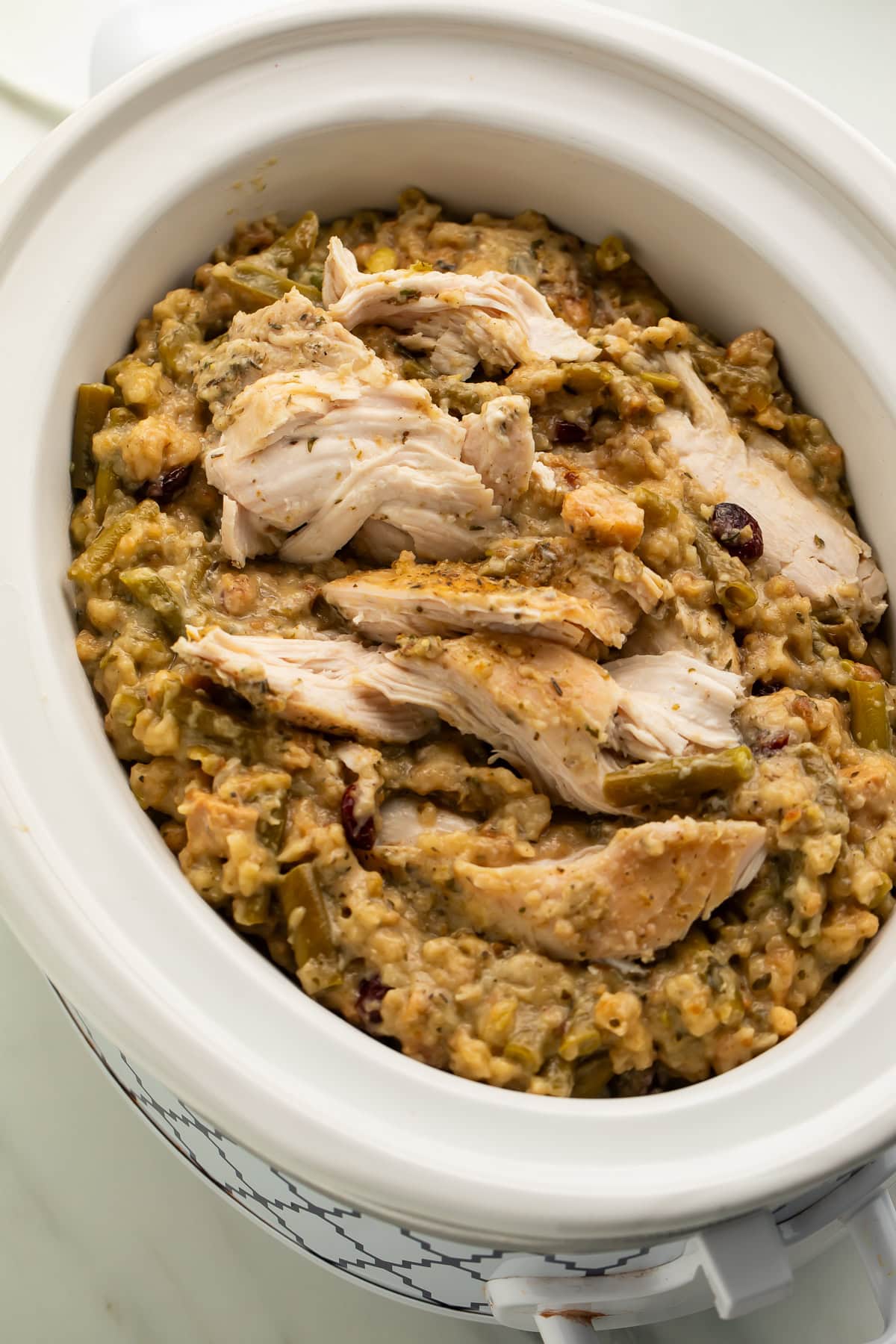Sliced chicken breasts on top of herb stuffing with green beans and cranberries in white crockpot insert