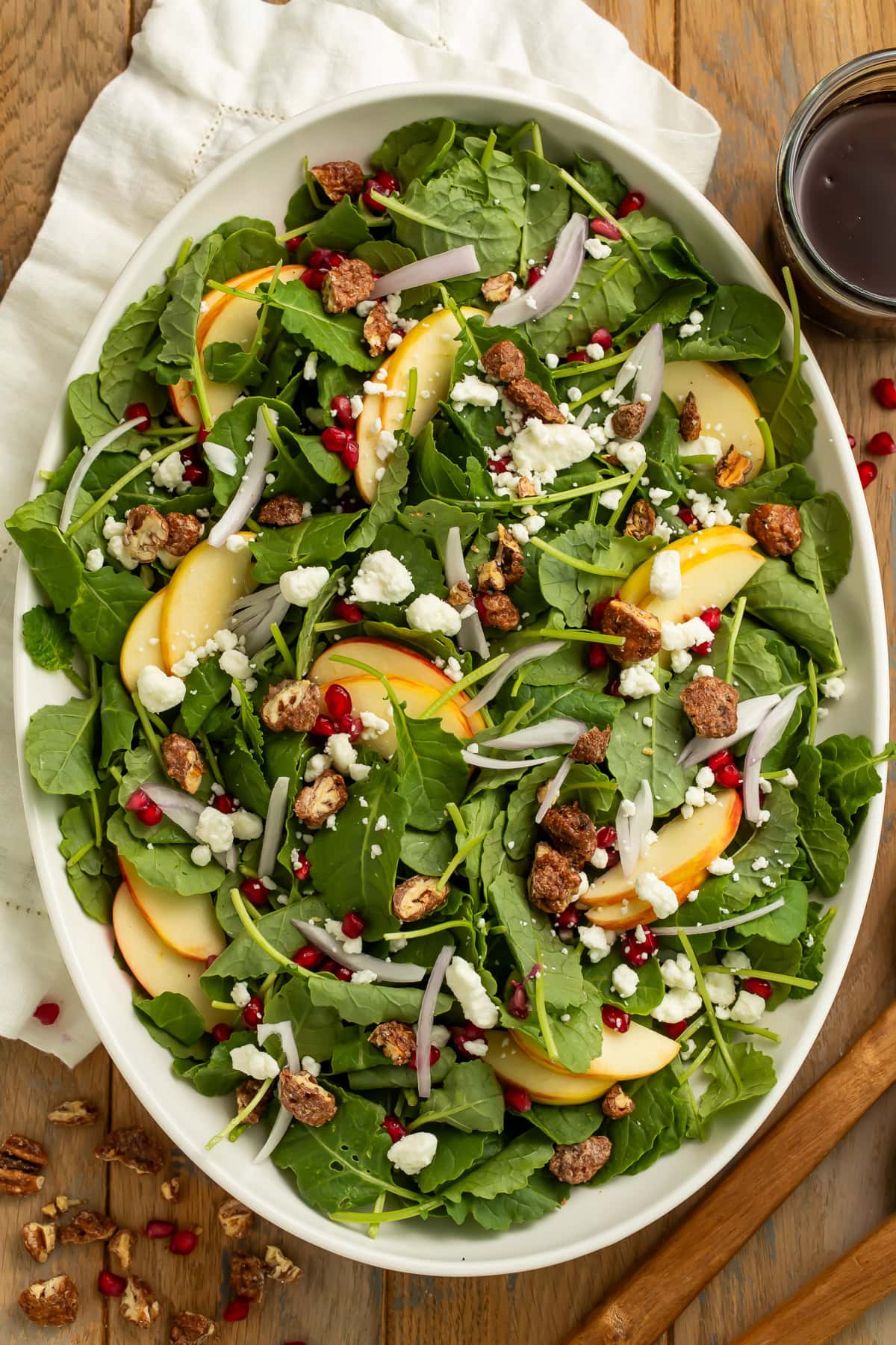 Christmas salad in white serving bowl on wooden board with arugula, pears, pomegranate, goat cheese, and pecans.