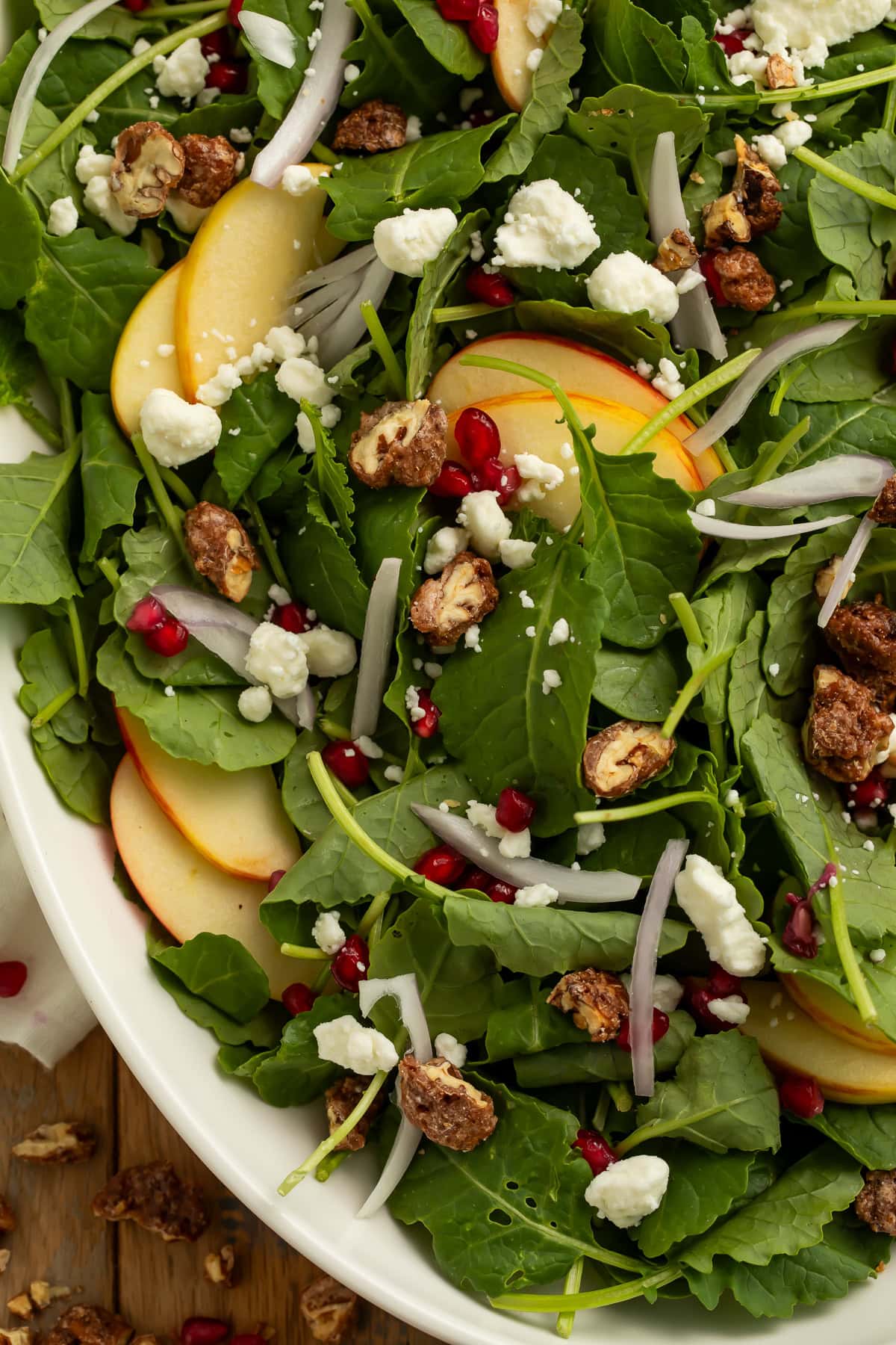 Close up overhead view of Christmas salad with arugula, apple slices, pomegranate arils, goat cheese, and candied pecans.