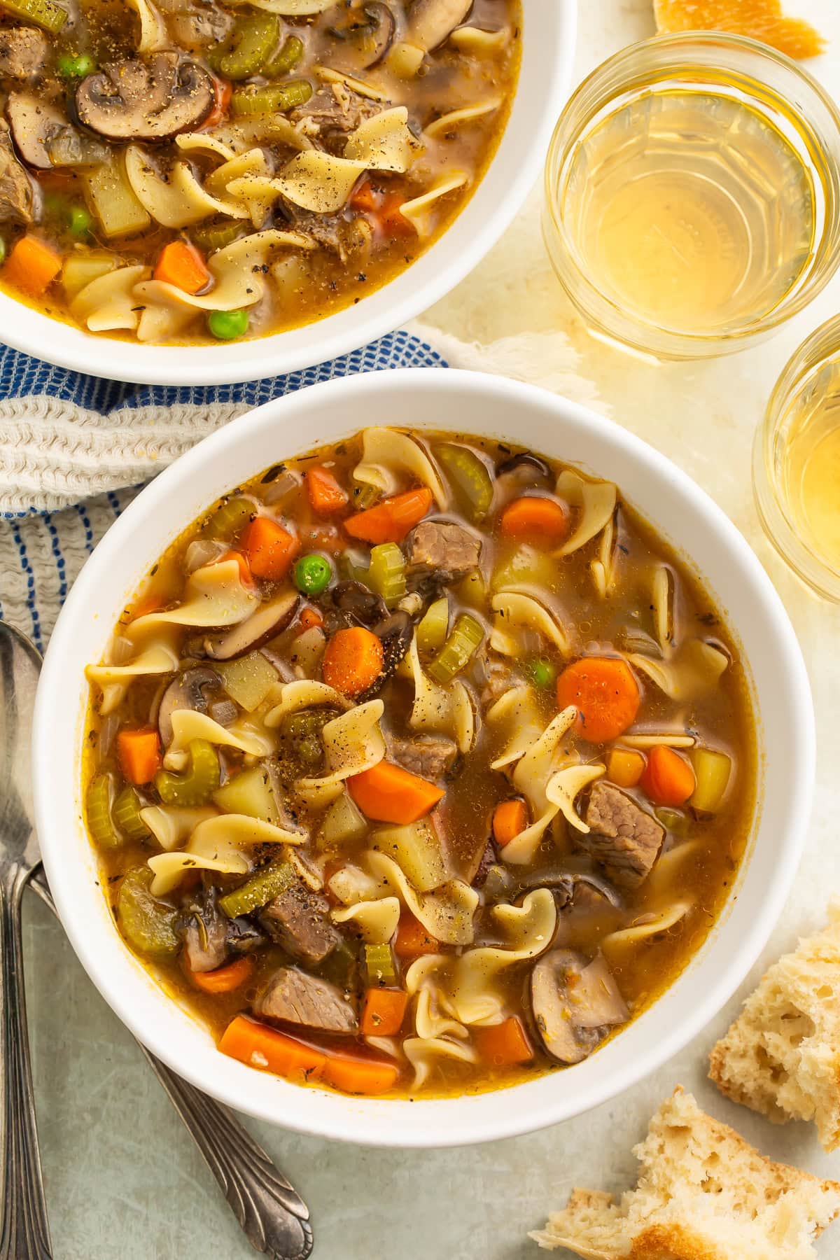 Close-up of white bowl with beef noodle soup showing chunks of meat, wide noodles, sliced carrots, and broth.