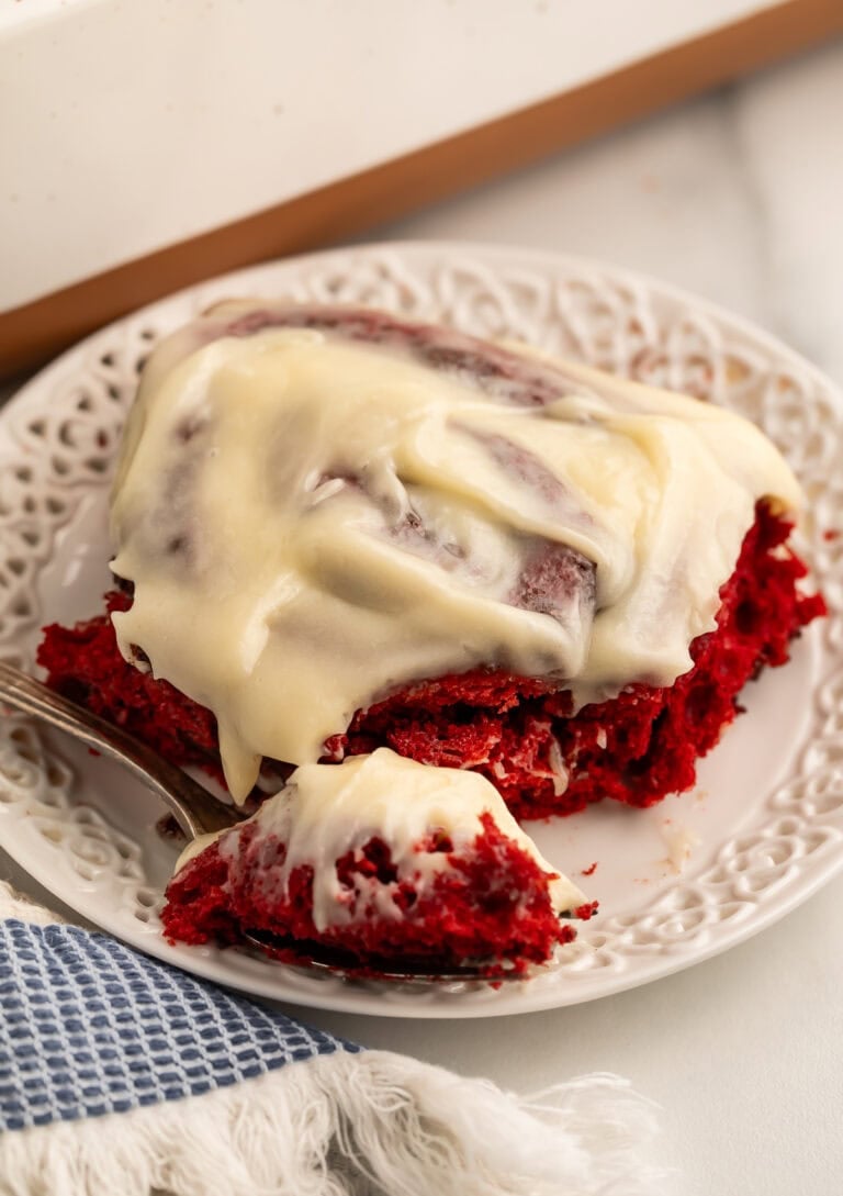 Single red velvet cinnamon roll on decorative white plate with fork and bite taken