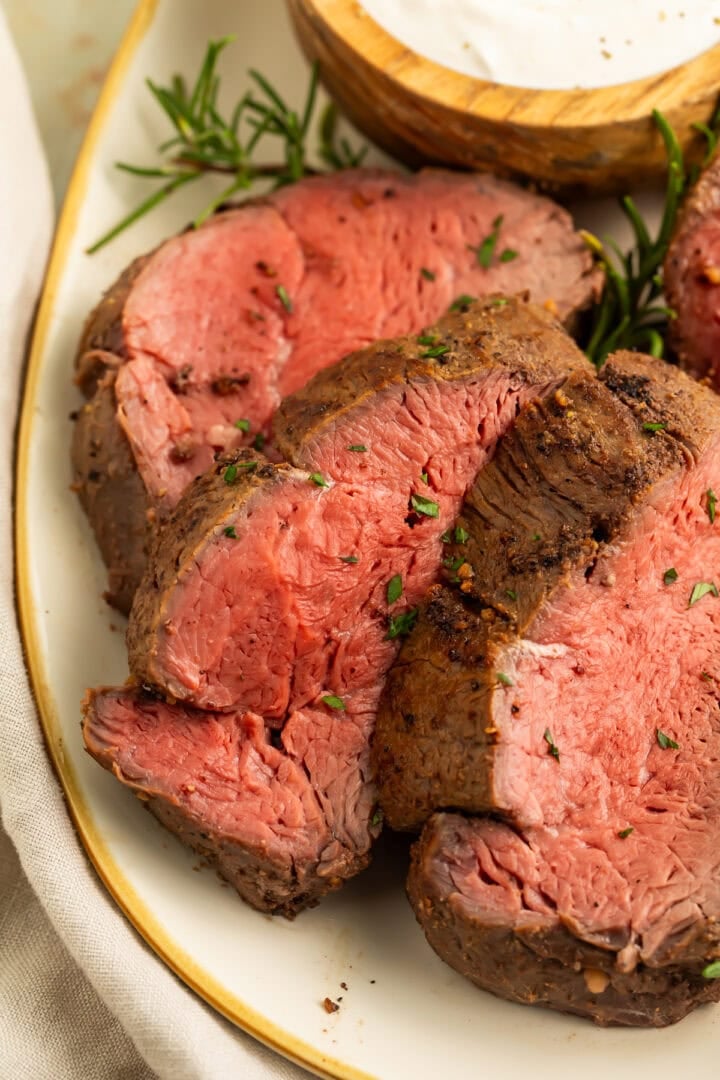 Sliced smoked beef tenderloin with pink medium-rare center and seasoned crust on white plate with gold rim