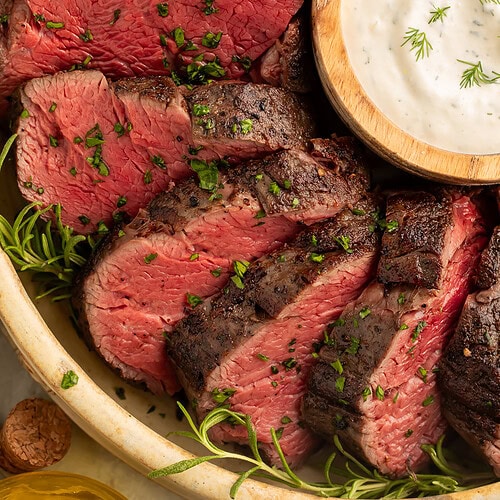 Sliced sous vide beef tenderloin with perfect medium-rare center and golden-brown crust, served with horseradish cream sauce and fresh rosemary.