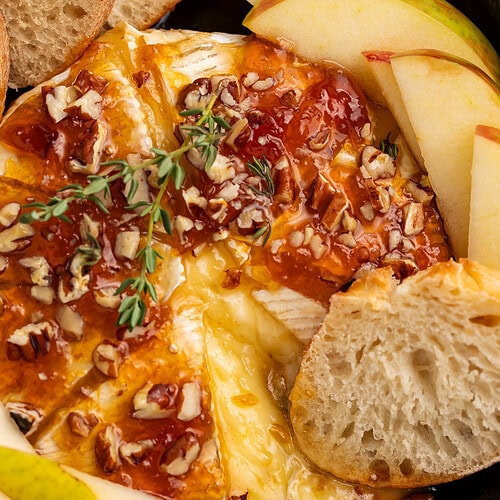 Baked brie with honey drizzle and chopped pecans in cast iron skillet with pear slices and bread