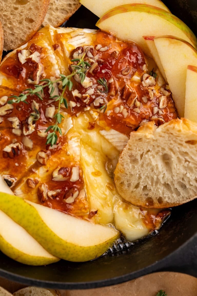 Baked brie with honey drizzle and chopped pecans in cast iron skillet with pear slices and bread