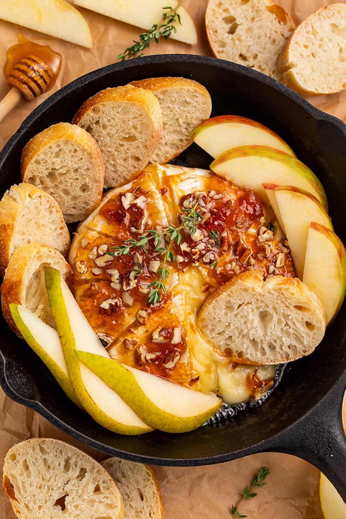 Overhead view of baked brie in cast iron skillet surrounded by bread and pear slices