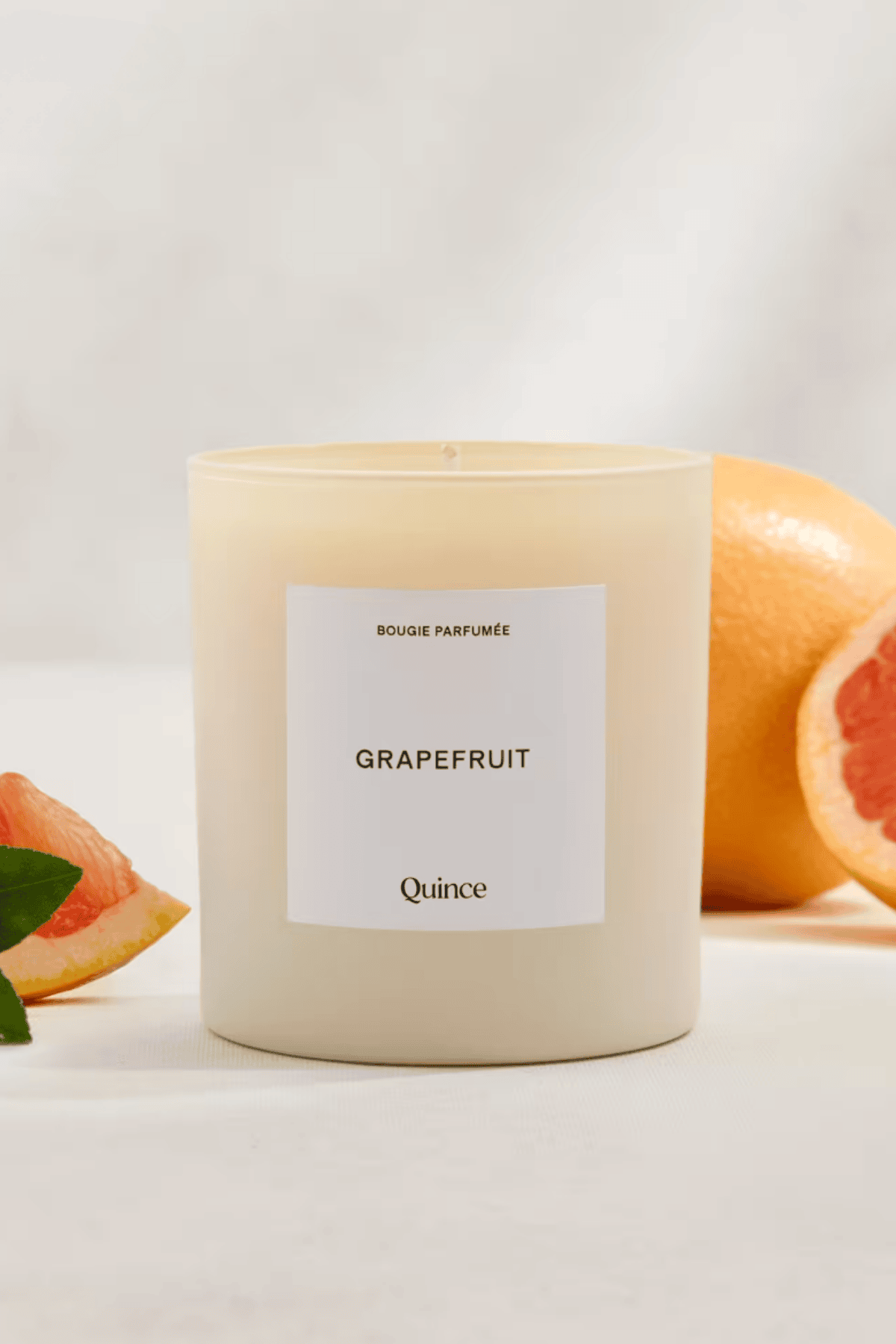 Quince grapefruit scented candle in frosted glass jar with fresh grapefruit