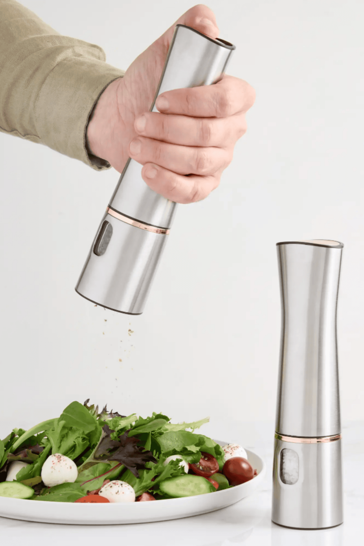 Hand holding Quince stainless steel electric pepper mill grinding seasoning over fresh salad